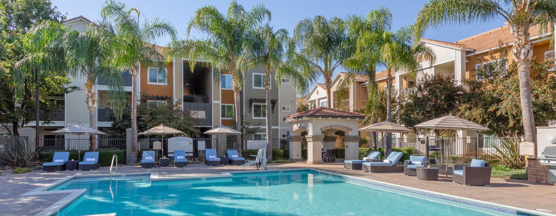 a pool with chairs and umbrellas by apartment building